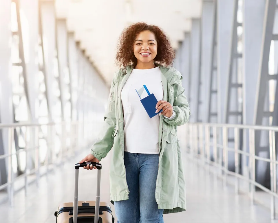 Mujer sonriente con su maleta y su pasaporte en un pasillo de aeropuerto